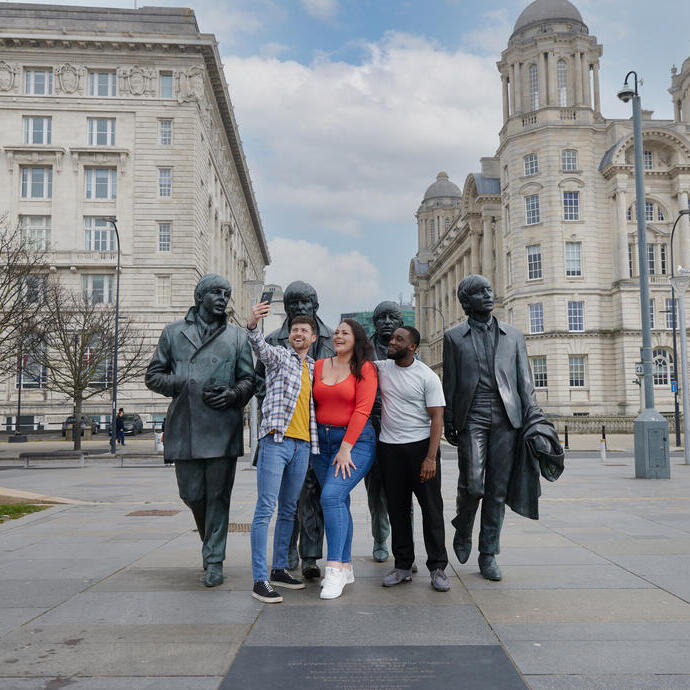 Eine Gruppe von Freunden, zwei Männer und eine Frau, machen ein Selfie vor einer Statue im Stadtzentrum.