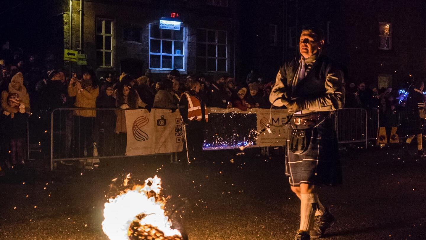 Un uomo che fa roteare una palla di fuoco su un bastone durante una parata a Stonehaven