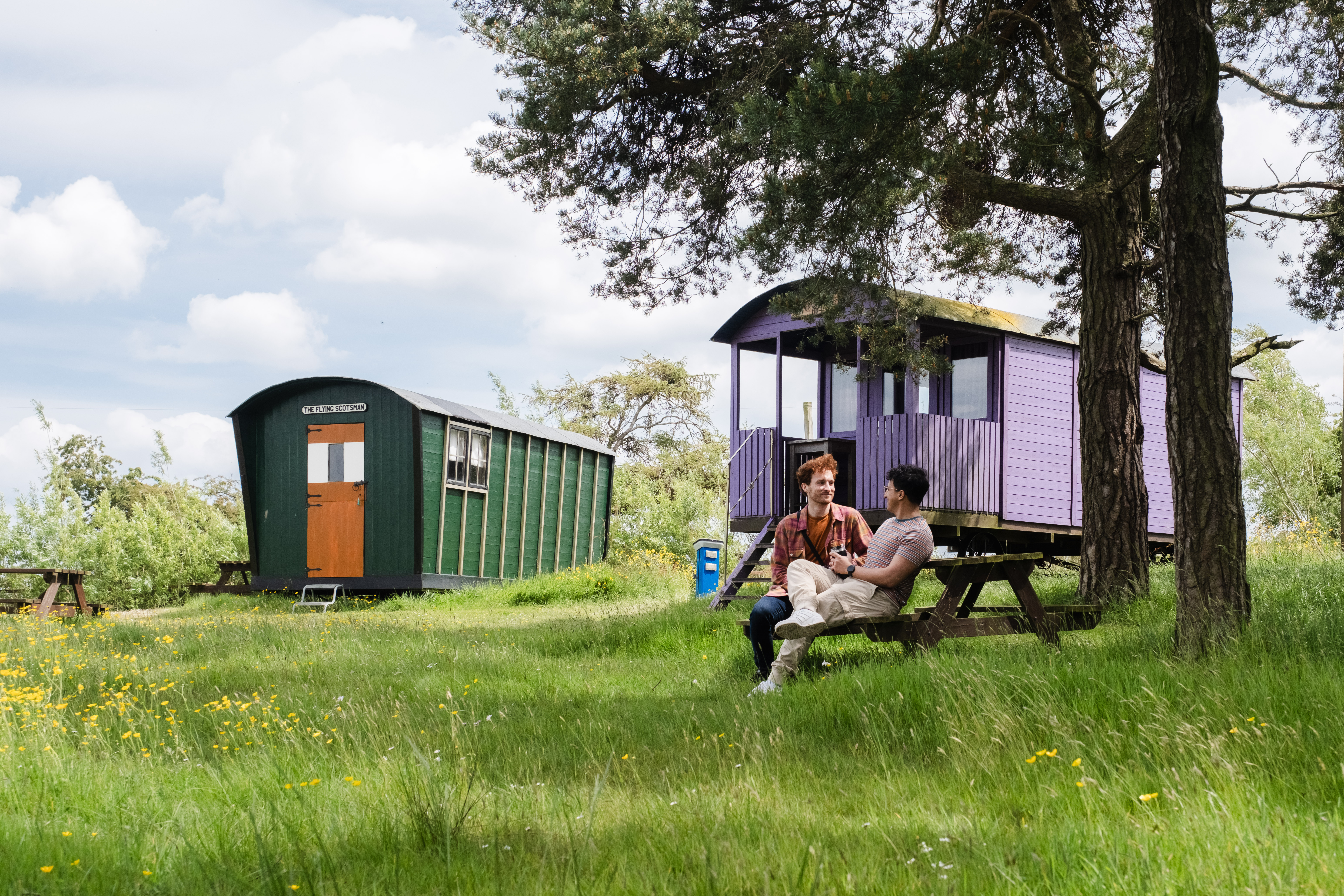 Two men sat oustide a shepherds hut in the countryside