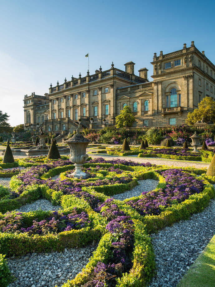 Jardin à la française avec statues et haies basses devant une maison majestueuse