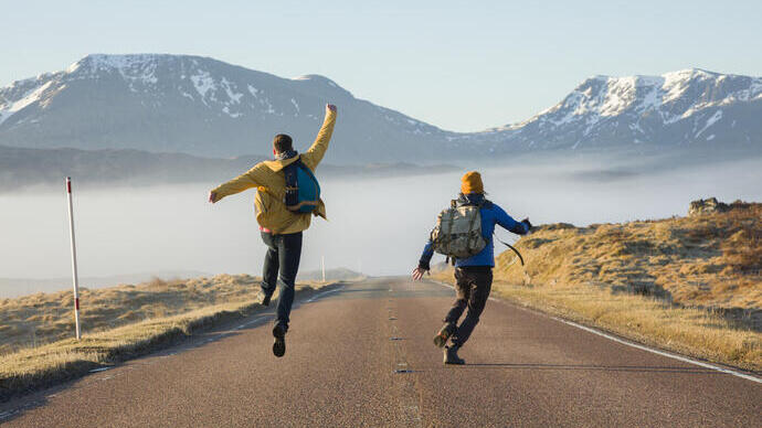 Two men walking and jumping on a road surrounded by mountains