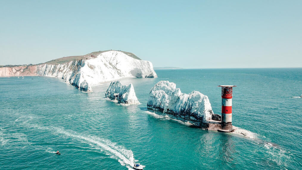 Tall chalk formations in a row running from the cliffs of the mainland to a lighthouse