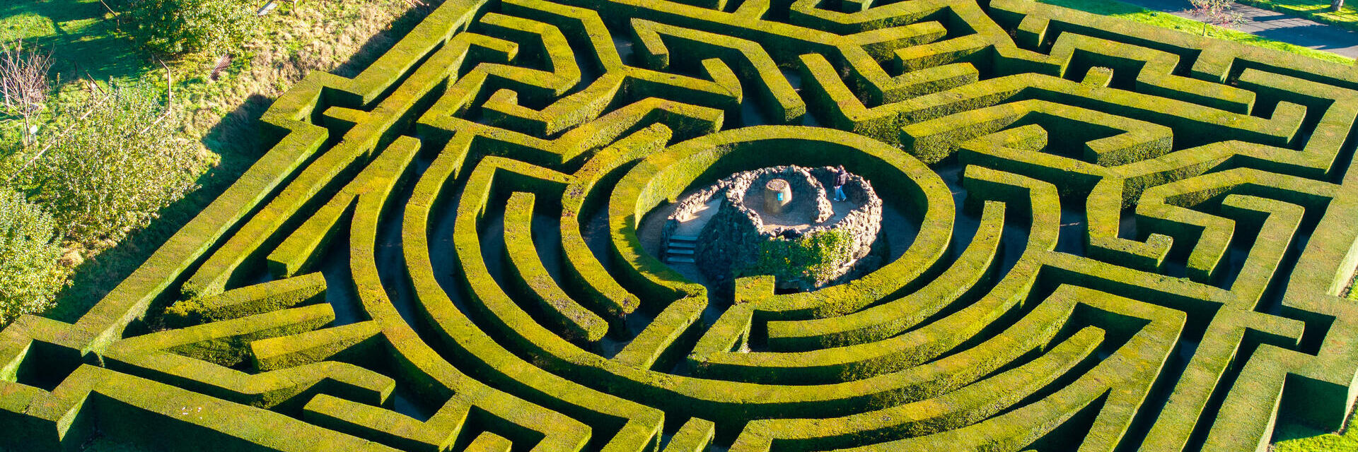 Luftaufnahme einer Frau, die den zentralen Turm eines Heckenlabyrinths hinaufsteigt