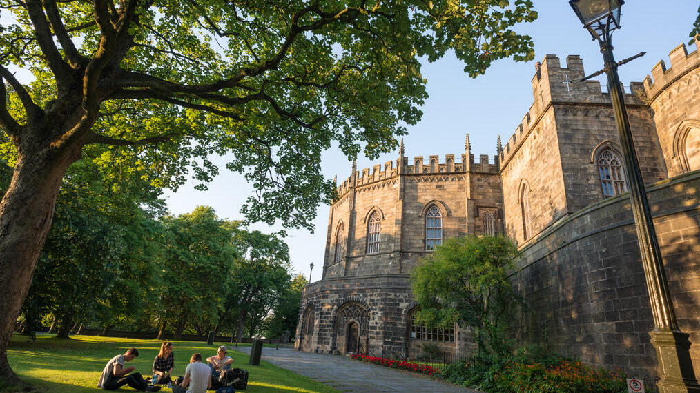 Außenansicht des Lancaster Castle mit Besuchern, die auf dem Rasen im Vordergrund sitzen