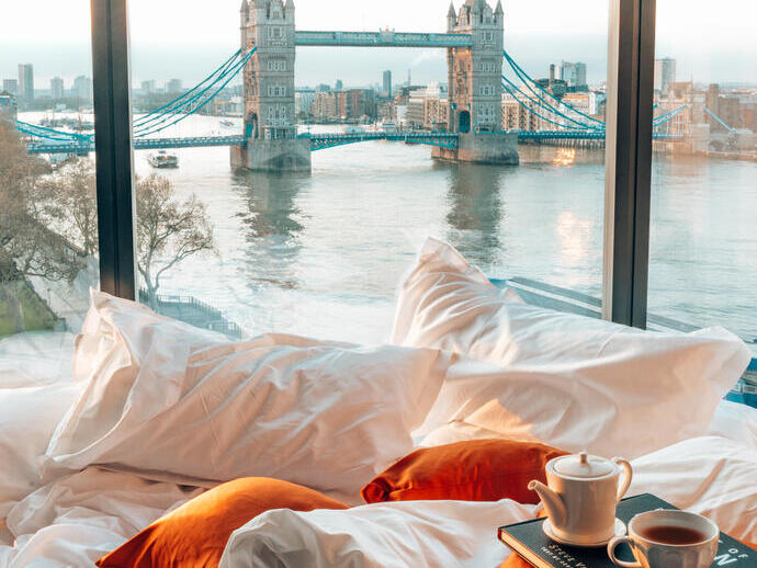A hotel bedroom with city views of a river and a bridge from the window
