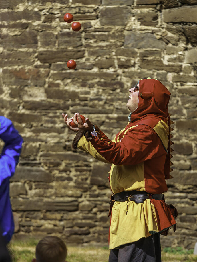 Un malabarista vestido con traje tradicional haciendo malabares con pelotas en el castillo de Conwy