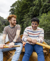 A male couple sitting in a rowboat, rowing together