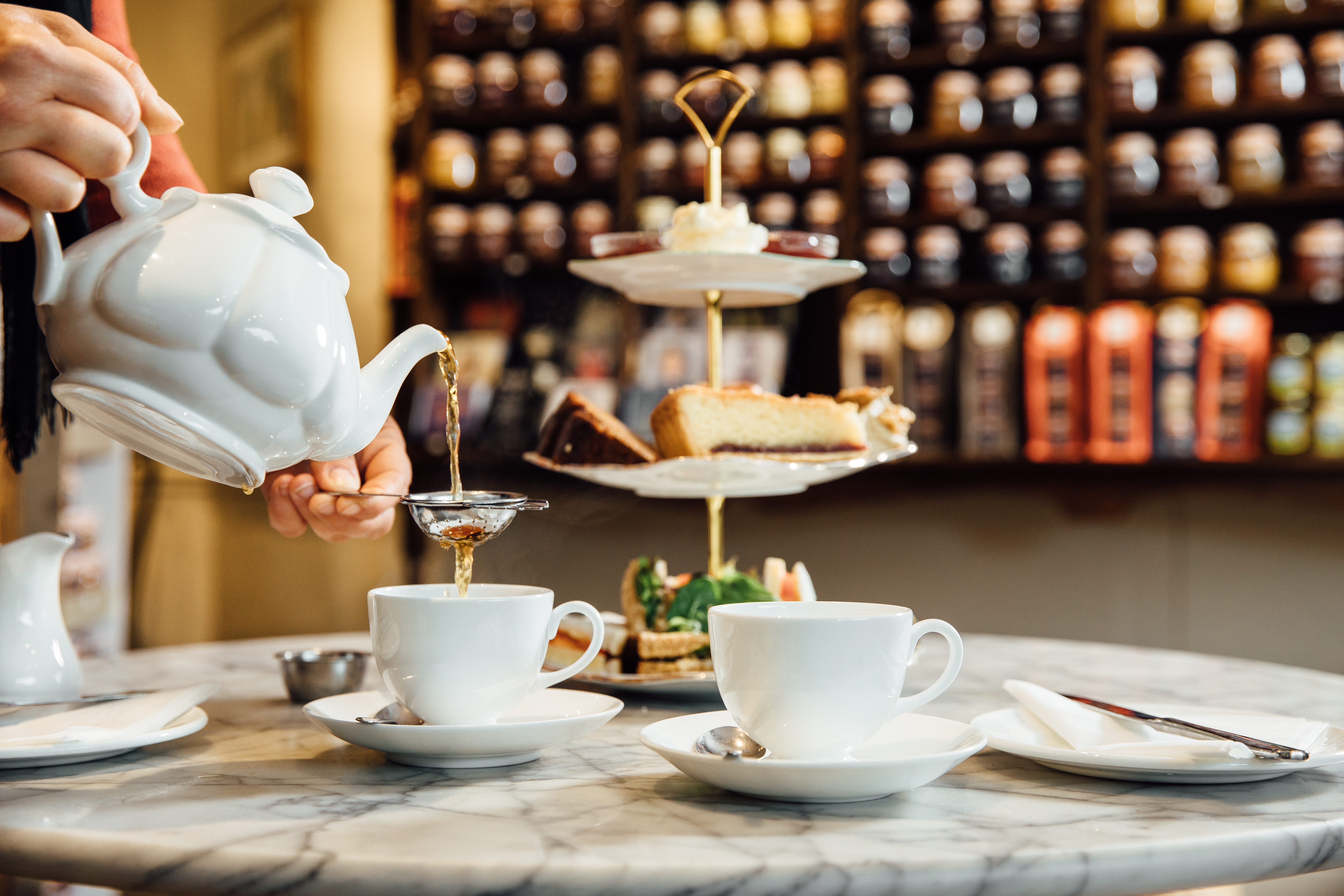 Person pouring cup of tea from white teapot in a tea shop
