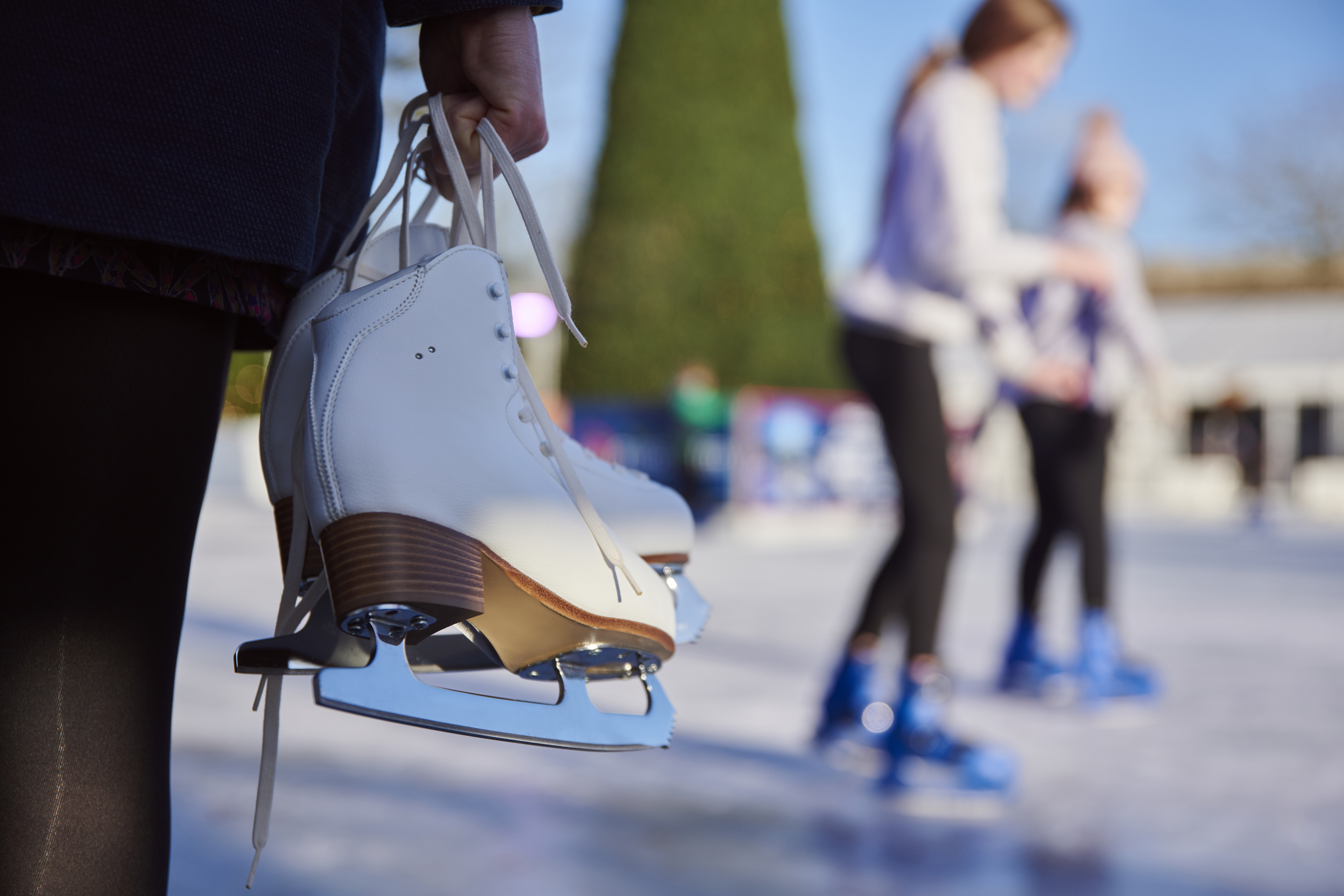 Hände, die ein Paar weiße Schlittschuhe an den Schnürsenkeln halten