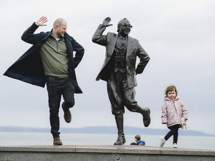 View of man, female child and statue of a man in front of the sea