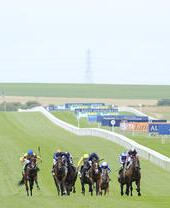 A group of horses and jockeys galloping flat out on Newmarket Racecourse, watched by spectators.