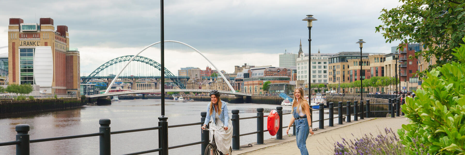 Zwei Menschen, die auf einem Weg entlang des Flusses Tyne in Newcastle Fahrrad fahren und Skateboard fahren.