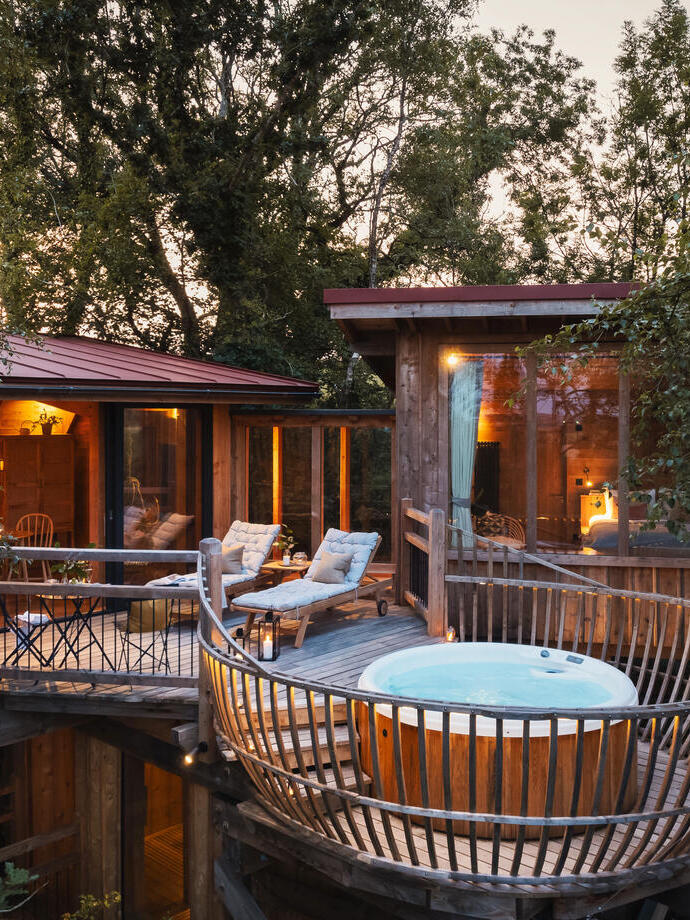 The external deck of the treehouses in the daytime with hot tub, sun loungers and lanterns at a luxury countryside treehouse retreat.