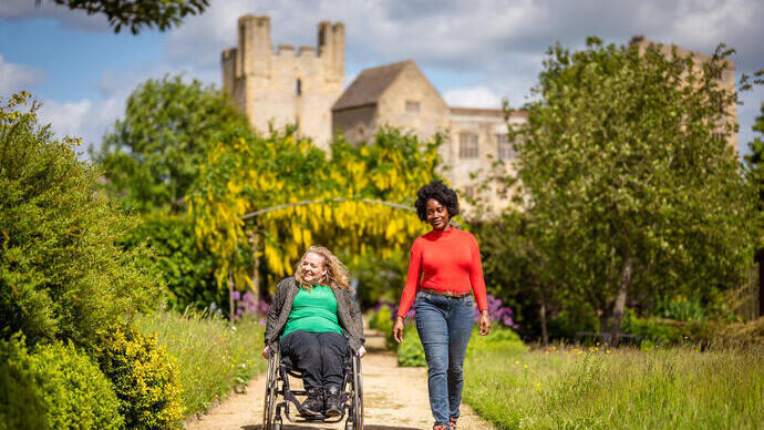 Dos mujeres caminando por un jardín con un castillo al fondo.