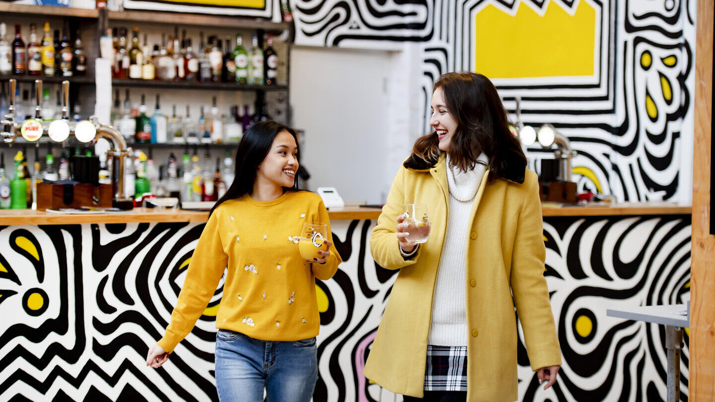 Zwei Frauen mit Getränken in der Hand, die sich von einer Bar entfernen