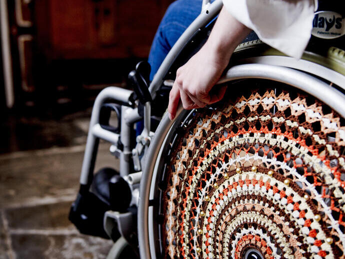 Frau im Rollstuhl neben Tudor-Wandbehängen in einem historischen Haus