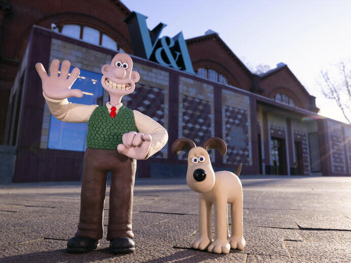 Deux personnages animés en pâte à modeler, un homme et un chien, debout devant un bâtiment victorien rouge.