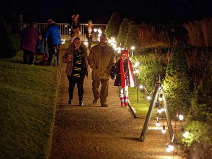 A family walking down a path lit up with fairy lights at night.