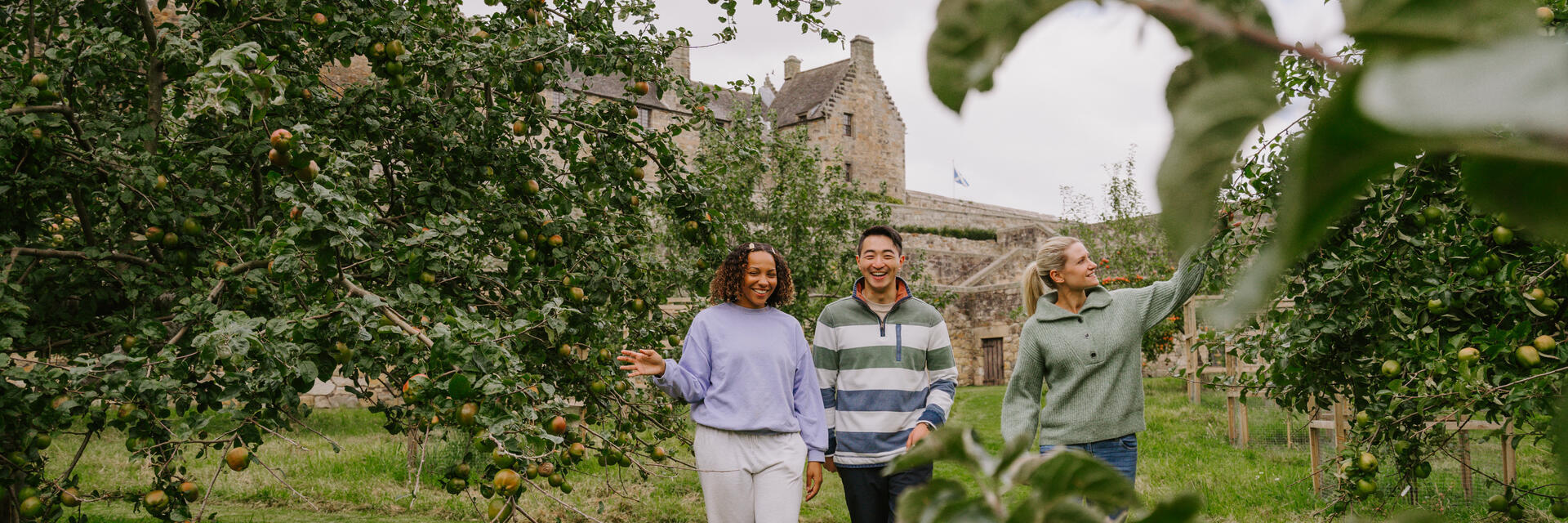 Un homme et deux femmes se promènent dans un verger de pommiers sur le domaine du château.