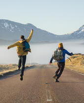 Two men walking and jumping on a road surrounded by mountains
