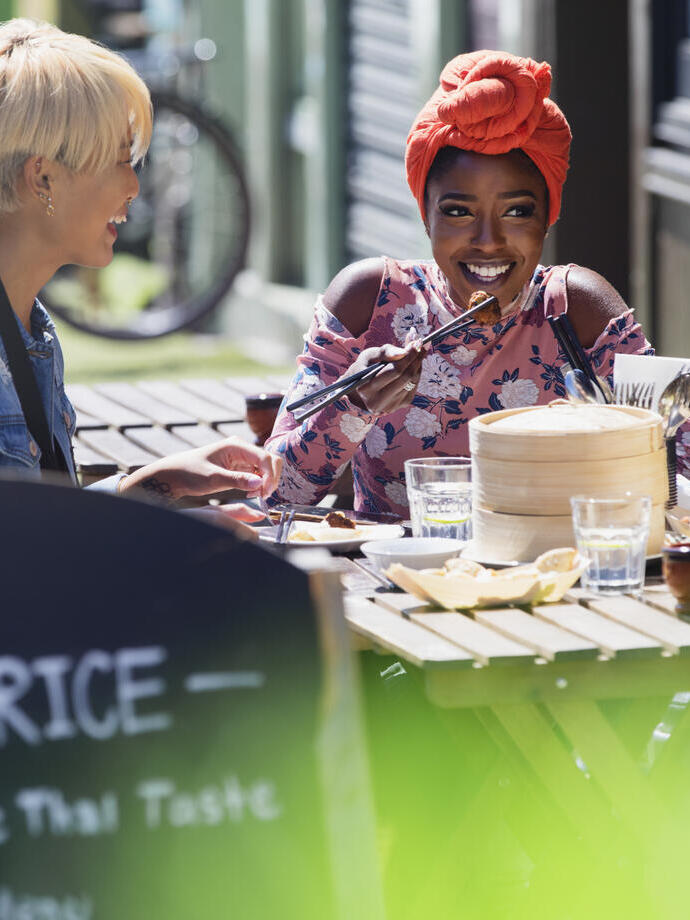 Three young women friends enjoying dim sum lunch at a sunny pavement cafe
