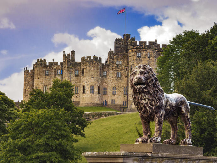 An historic castle with a UK flag at full mast and with a lion statue out the front.