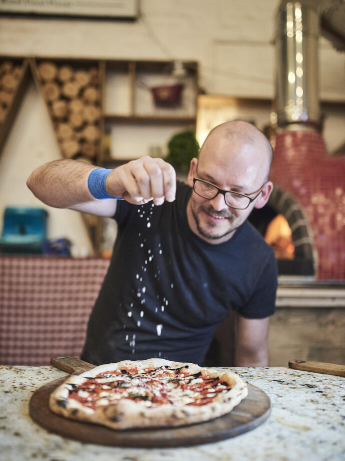 Man sprinkling cheese on pizza at a food market