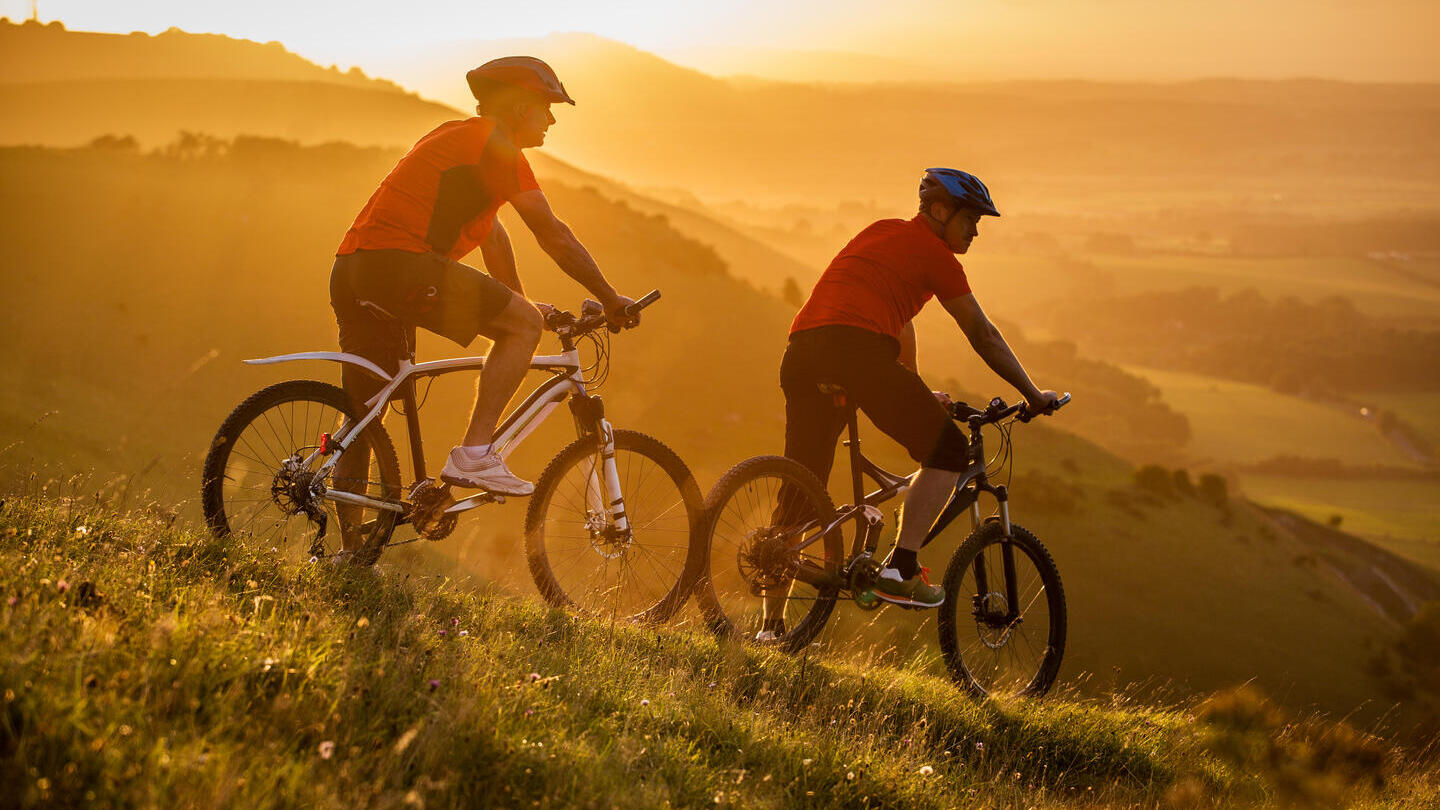 Two men on mountain bikes resting on the side of a hill at sunrise