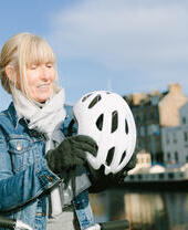 A woman putting on her bike helmet by the riverfront on a sunny day
