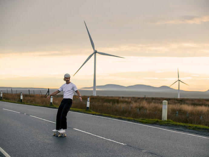 Man skateboarding on a road with wind turbines behind him