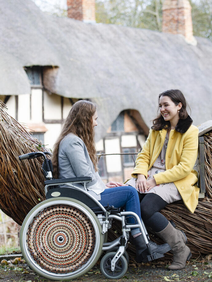 Frau im Rollstuhl und Freundin sitzen auf einem Sitz aus geflochtenem Korbgeflecht