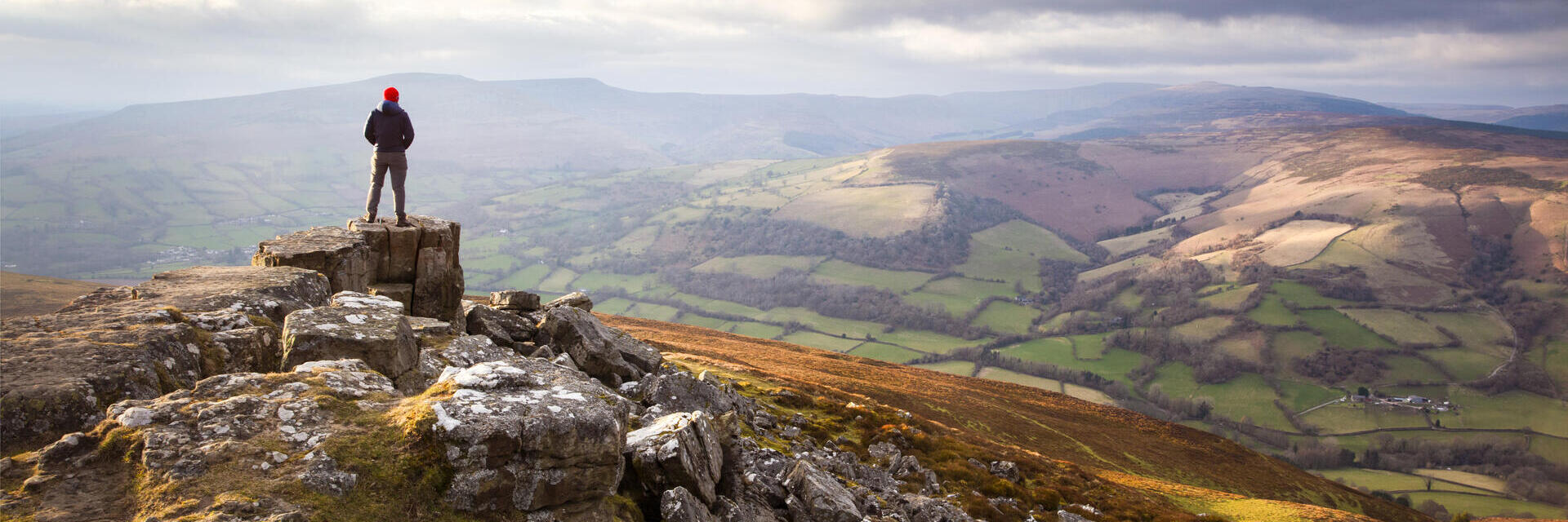 Hombre en lo alto de una vasta y colorida cordillera al atardecer contemplando el valle