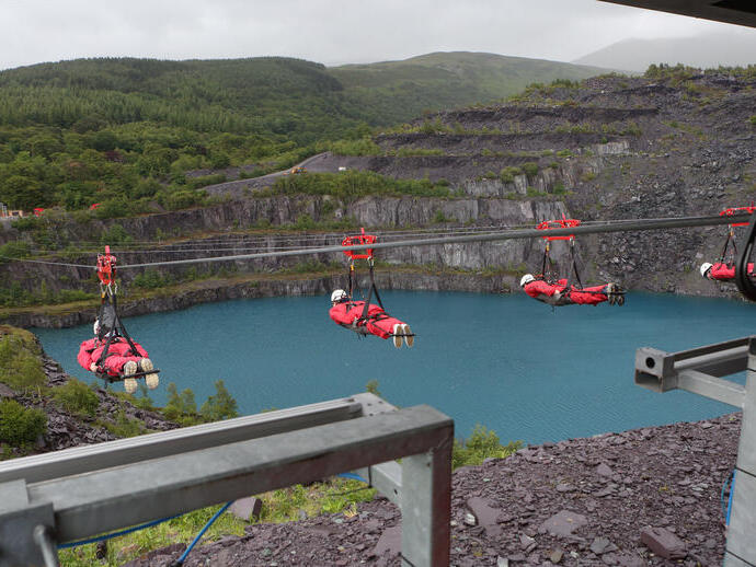 People ziplining across a large water filled quarry
