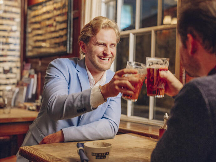 Deux hommes assis dans un pub trinquant avec des pintes de bière