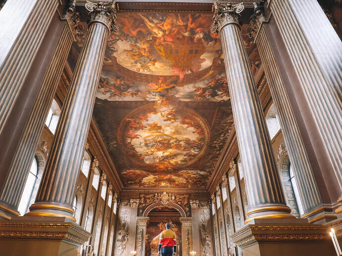 Man walking up a grand staircase towards a large hall with a painted ceiling