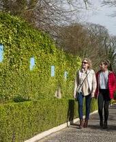 Two women walking along an hedge in a park