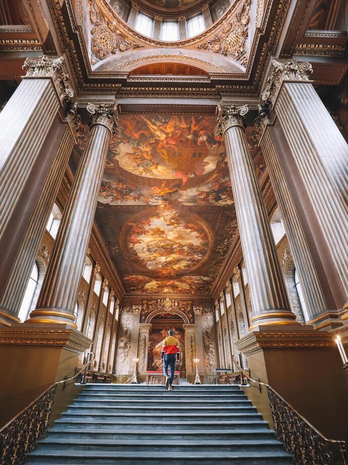Mann, der eine große Treppe hinauf zu einem großen Saal mit bemalter Decke geht