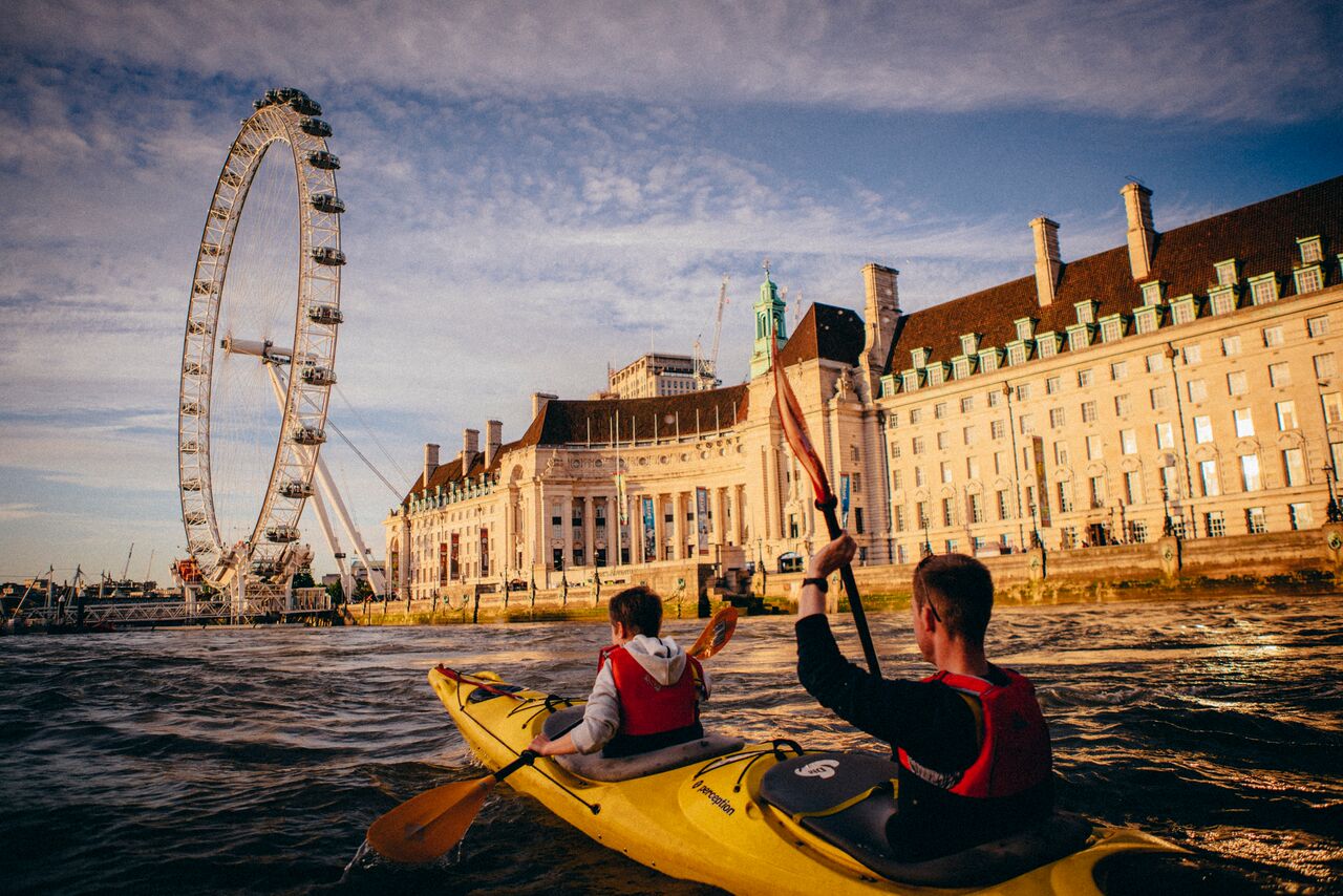 Deux personnes font du kayak sur la Tamise, avec le London Eye et un bâtiment historique en arrière-plan.