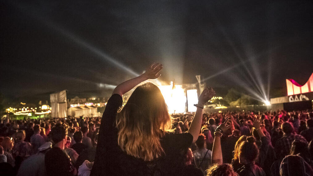 Mujer entre la multitud en un concierto de música con los brazos en alto viendo una actuación