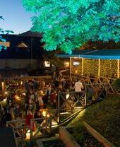 Des personnes mangeant et buvant à des tables dans le jardin du Brel's Garden Area, le soir