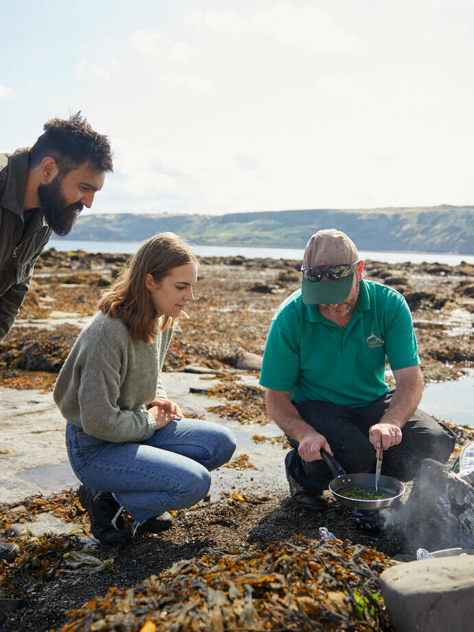 Trois personnes parmi les rochers au bord de la mer, l'une d'elles est en train de cuisiner