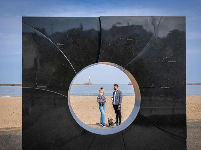 Two people seen through an art display on a beach sculpture trail.