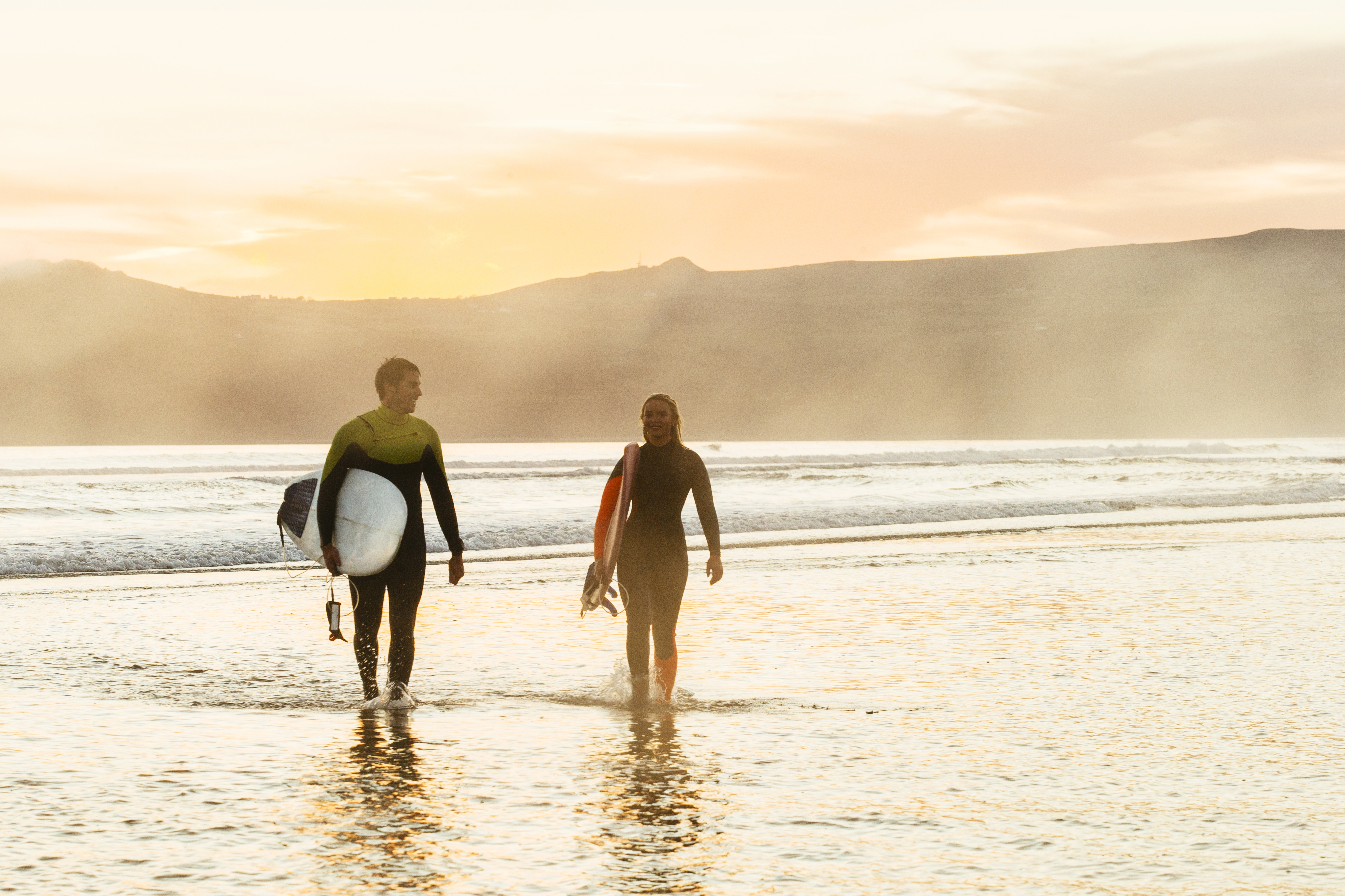 Uomo e donna che trasportano tavole da surf e escono dal mare