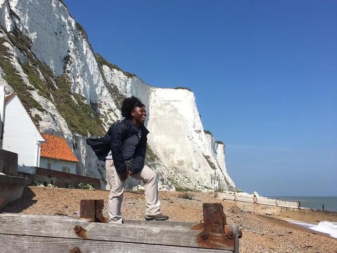Woman standing on wooden groynes on a beach with white cliffs behind
