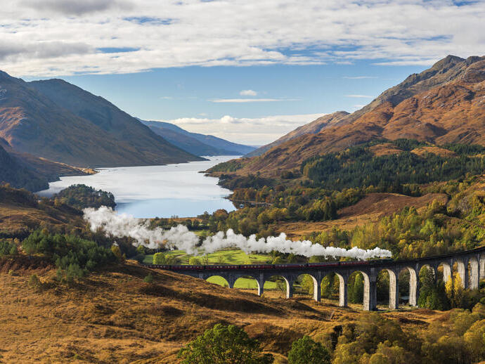Blick auf das Tal in den Highlands und das Glenfinnan-Viadukt, Dampfzug auf den Gleisen, Loch Shiel im Hintergrund