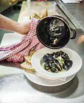 A chef plating up a bowl of mussels in a restaurant.