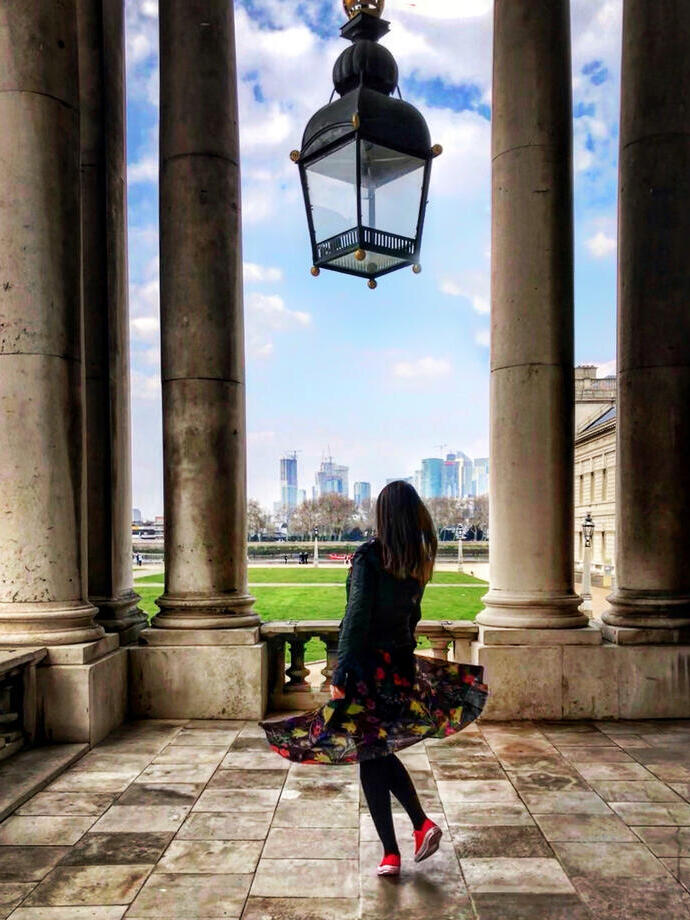Woman standing underneath a large glass lantern, looking through the colonnades towards modern city buildings