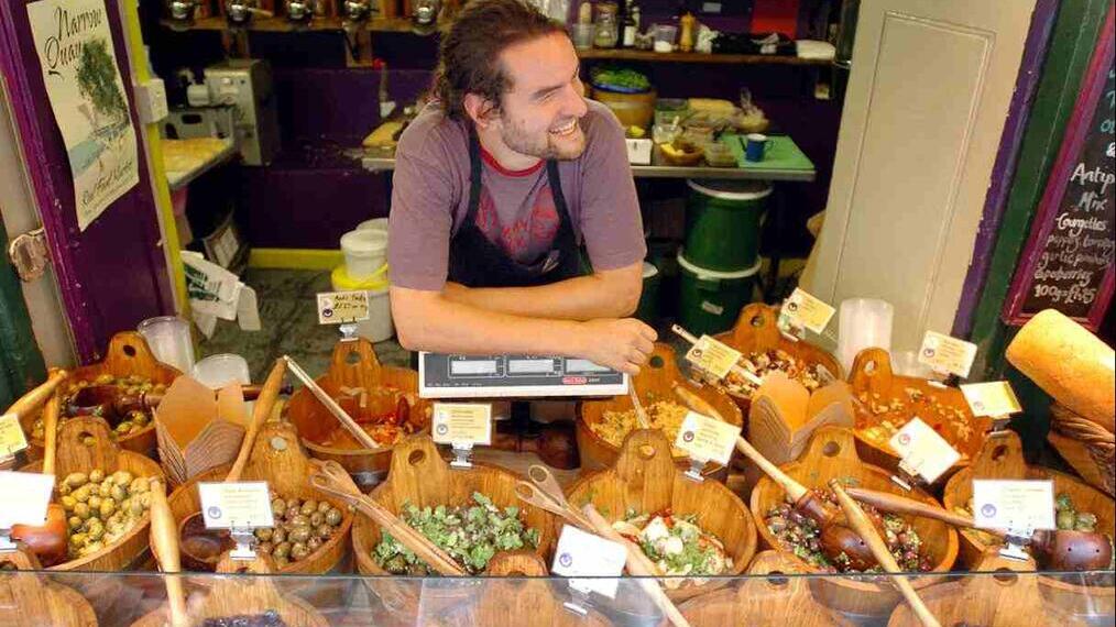 A market trader selling many varieties of olives from a stall