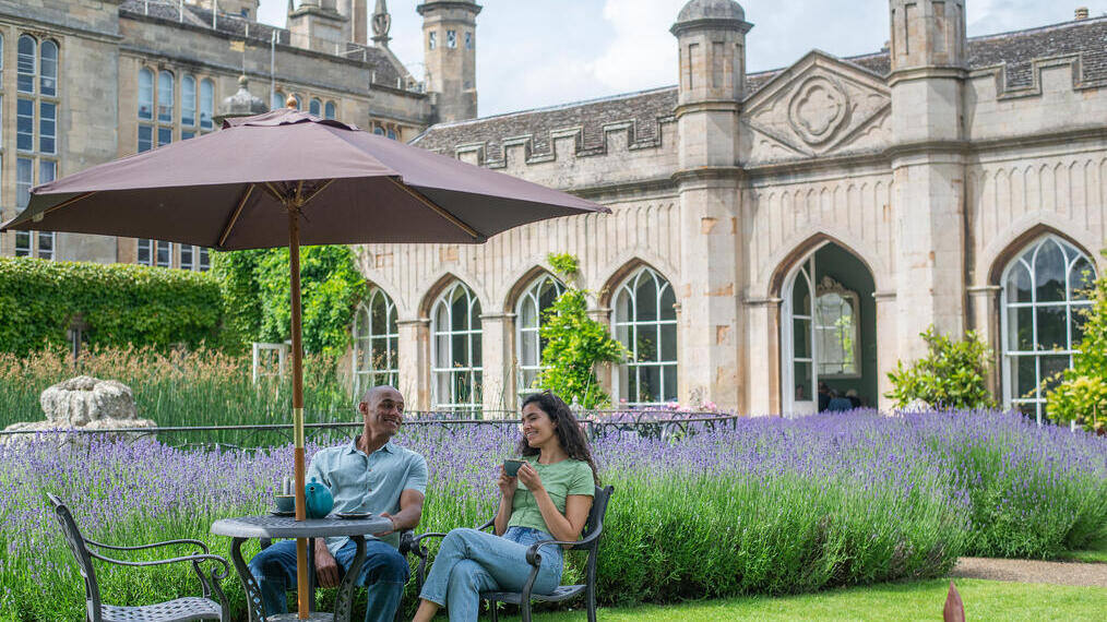A man and a woman drink tea together in the gardens of a heritage house