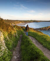 Walker traversing a coastal beach path overlooking a large empty beach.